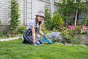 Woman in sun hat kneeling down and working in her garden smiling
